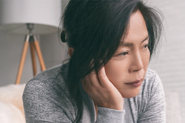 Adrenal-Fatigue-Doctor A middle-aged asian woman sitting on her couch, resting her head on her hand, suffering from adrenal fatigue. Get treatment for adrenal fatigue syndrome from Julie Kane, NP of Bird Island Wellness in Calgary.