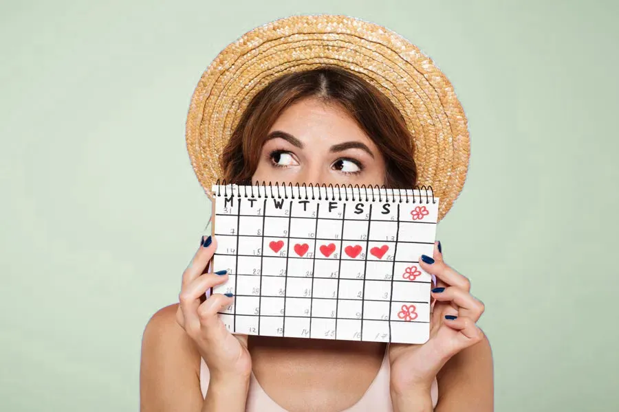 Menstrual-Dysfunction-Doctor A woman in a straw hat holds a calendar with several days marked off in front of her nose and mouth. Get treatment for menstrual dysfunction from Julie Kane, NP of Bird Island Wellness in Calgary.