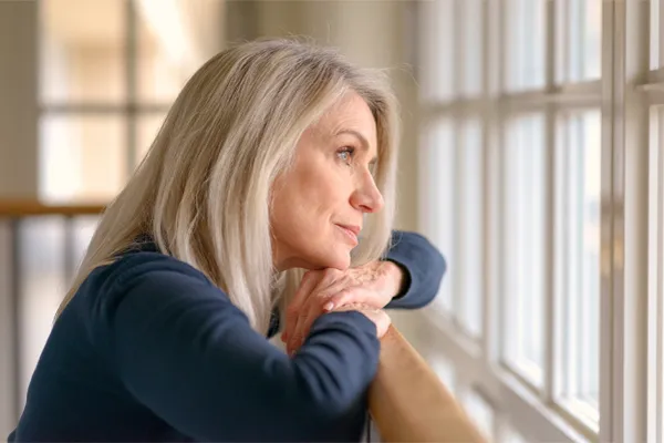 PMDD-Specialist A middle-aged woman with with a somber expression stares out the window. Get treatment for Premenstrual Dysphoric Disorder from Julie Kane, NP of Bird Island Wellness in Calgary.