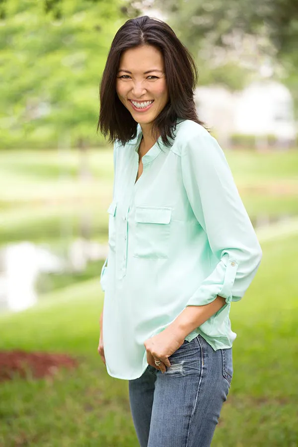 Perimenopause-Treatment A middle-aged brunette woman in a light green button-up shirt stands outside smiling, happy with her perimenopause treatment from Julie Kane, NP of Bird Island Wellness in Calgary.