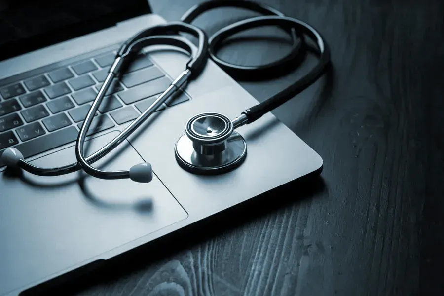 Telemedicine-Doctor An open laptop with a stethoscope lying on it on a wooden table, symbolizing telemedicine care from Julie Kane, NP of Bird Island Wellness in Calgary.