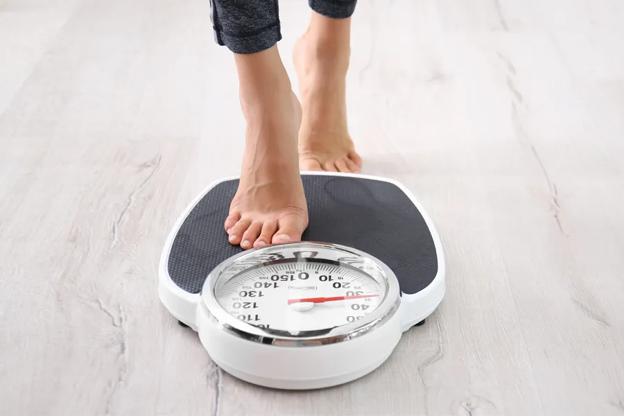A woman steps on to a scale to weigh herself. Get low dose naltrexone for weight loss treatment from Julie Kane, NP of Bird Island Wellness in Calgary.