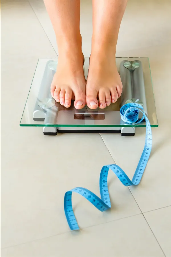Weight-Loss-Resistance-Treatment Close-up of a woman's feet standing on a scale, with measuring tape by her toes, getting treatment for weight loss resistance from Julie Kane, NP of Bird Island Wellness in Calgary.